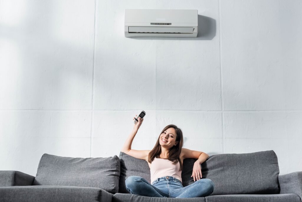 attractive and smiling woman switching on air conditioner with remote controller