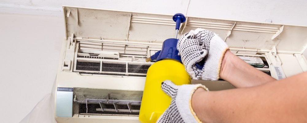 Technician spraying chemical water onto air conditioner grid to